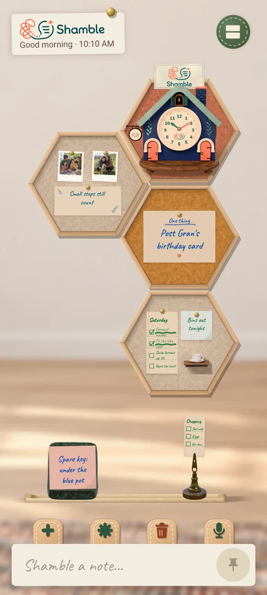 Shamble on a phone with the board rearranged into a tall column of four felt hexagons: the clock cottage, two photos, the One Thing card and a Saturday checklist, with the shelf below holding a spare-key note and a shopping list